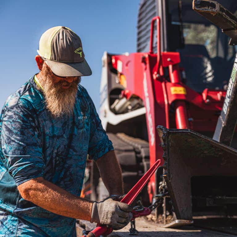 man strapping down a skid steer disc mulcher belt drive