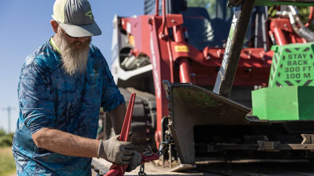 man removing straps off of skid steer that has a disc mulcher belt drive