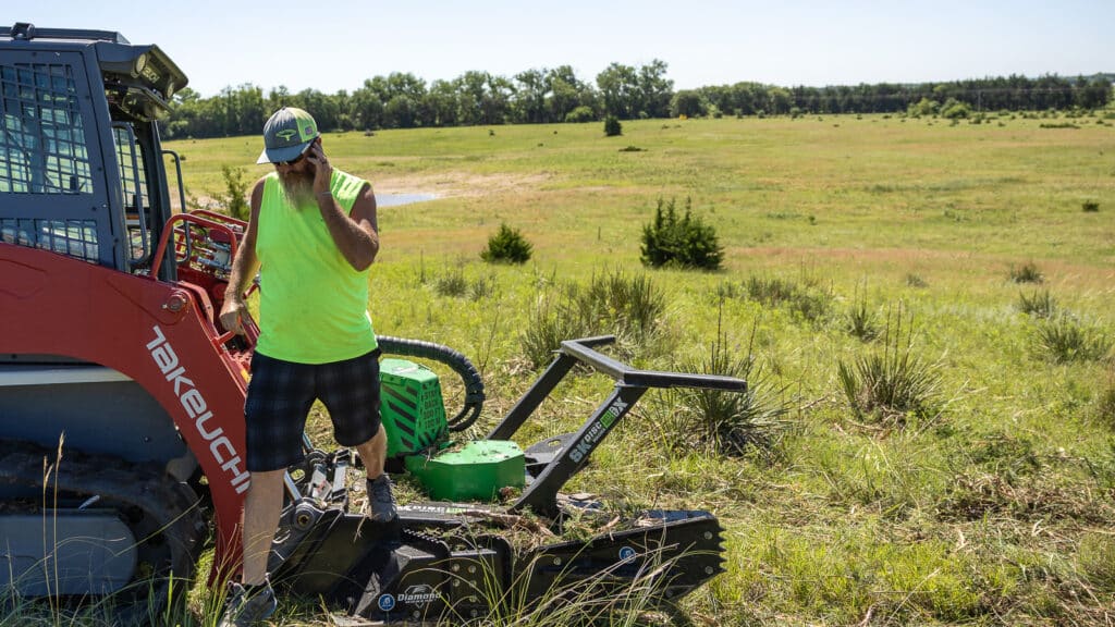 man stepping out of skid steer that has a disc mulcher belt drive