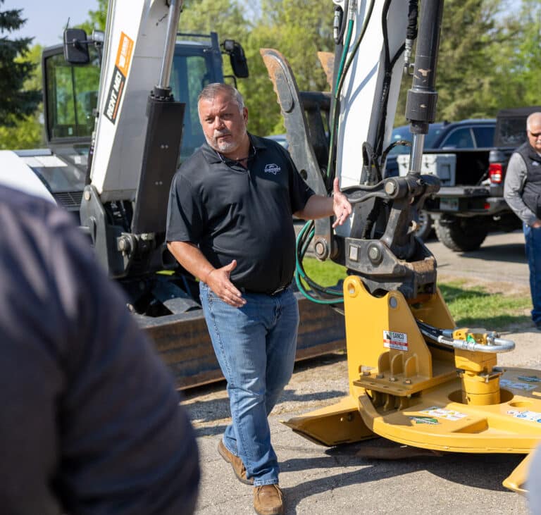 person showing a group of people how to use an excavator brush cutter